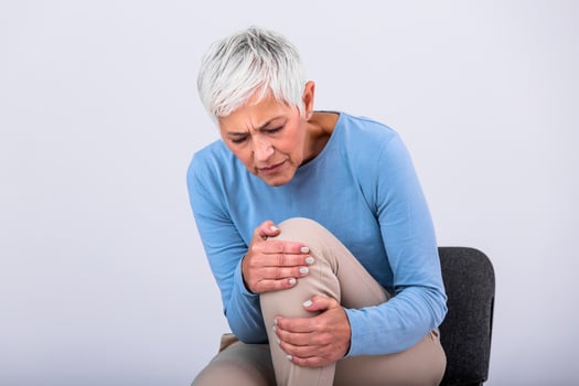 Senior woman holding the knee with pain. Old age, health problem and people concept - senior woman suffering from pain in leg at home. Elderly woman suffering from pain in knee at home photo