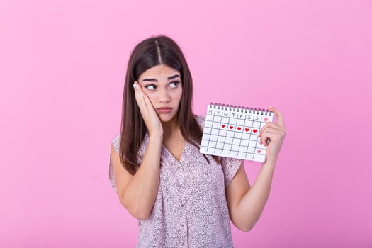 Young beautiful woman holding menstruation calendar over isolated background with surprise face. Young girl holding menstruation calendar with confused face, afraid and excited with fear expression photo