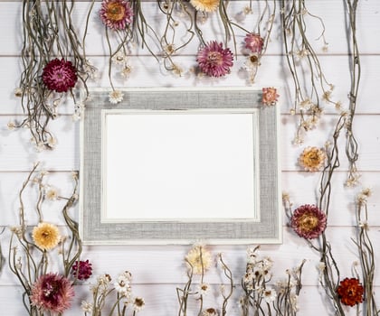 Top view of empty photo frame with dry colorful flowers over a white wooden table