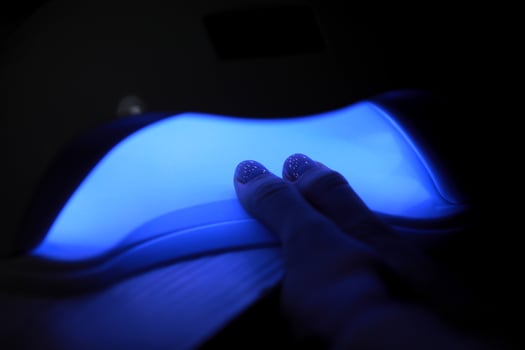 Closeup view of female hands with gel polish manicure. Woman puts hand into led uv lamp for curing top cover of nailpolish. UV lamp, LED Nail photo