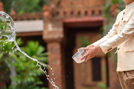 Young man splashing water from bowl on Songkran festival photo