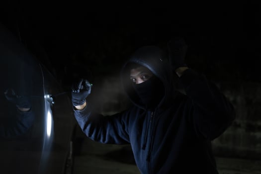 Young thief in black is stealing a car at night. He carries a flashlight and a screwdriver for car theft. photo