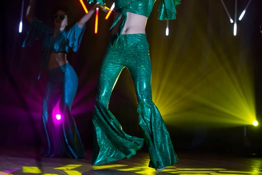 On the concert stage, illuminated by multi-colored beams, women's legs in 80s disco bell-bottoms. photo