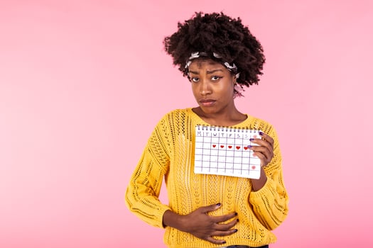 Young African American woman suffering from belly pain and showing her periods calendar isolated over pink background. Medical, healthcare, gynecological concept. Copy space photo