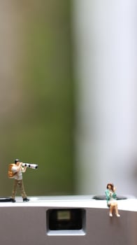 a miniature figure taking picture with a camera against a real camera in the background. photo