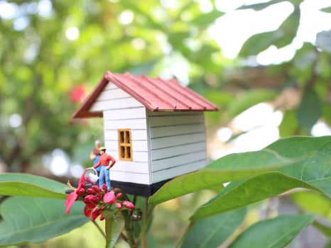 a close up of a miniature figure of a mother watering the plants in front of the house. photo