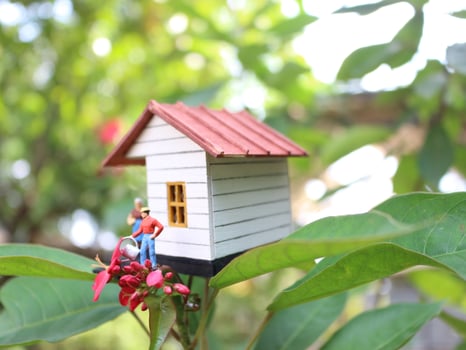 a close up of a miniature figure of a mother watering the plants in front of the house. photo