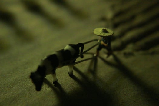 miniature figure of a farmer plowing a field with his cow on a cardboard. photo