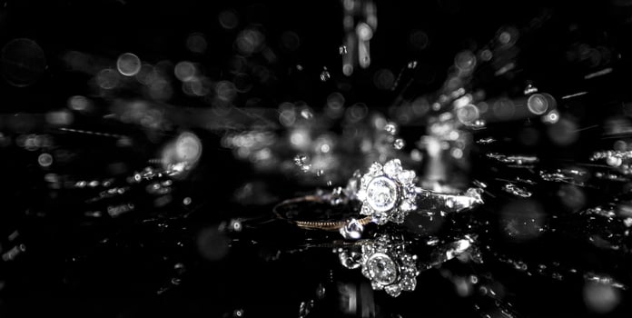 A diamond engagement and a wedding ring on a reflective surface with water splashing down from above. photo