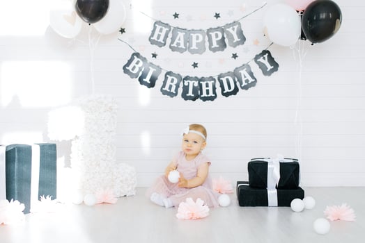 The birthday girl 1 year old sits on the photo zone and holds a ball in her hands