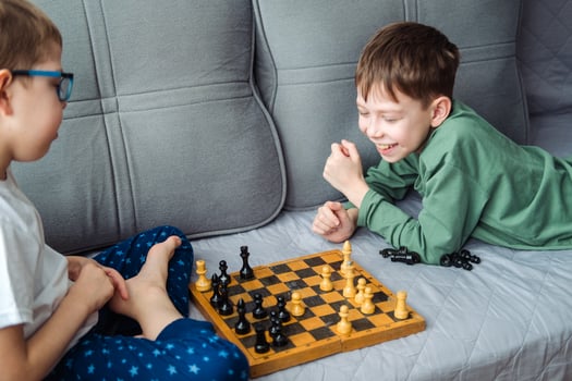 Boys play wooden chess lying on a gray sofa. photo
