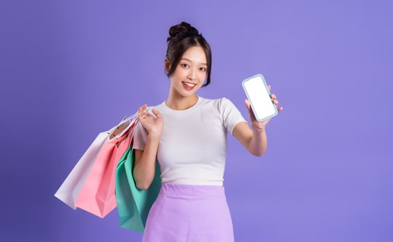 beautiful Asian girl holding shopping bag posing on purple background photo