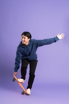 Image of young Asian man playing skateboard on purple background photo
