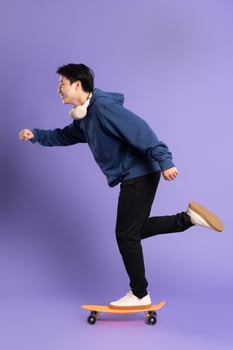 Image of young Asian man playing skateboard on purple background photo