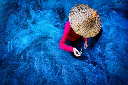 Women fisherman hands sewing blue fishing nets sitting on the ground and surrounded big net photo