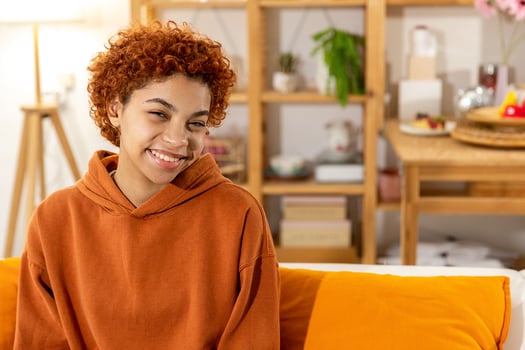 Beautiful african american girl with afro hairstyle smiling sitting on sofa at home indoor. Young african woman with curly hair laughing. Freedom happiness carefree happy people concept. photo