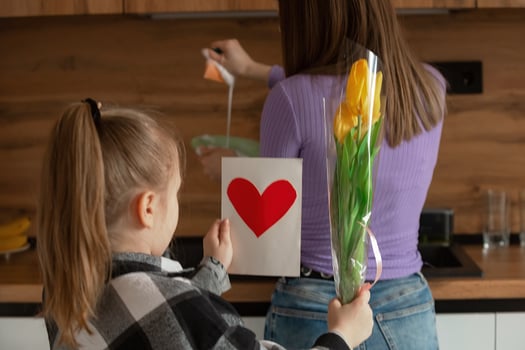 Daughter congratulates mom on Mother's Day, card with heart and flowers. A woman washes dishes and is busy with household chores. photo