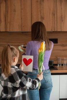 Daughter congratulates mom on Mother's Day, card with heart and flowers. A woman washes dishes and is busy with household chores. photo