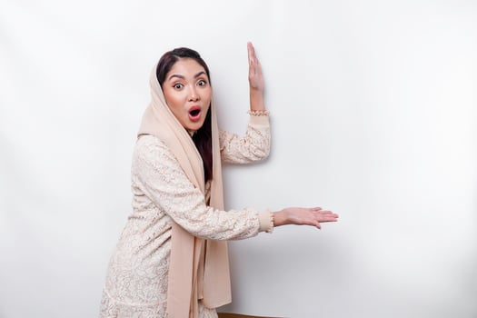 Shocked Asian Muslim woman pointing at the copy space on beside her, isolated by white background photo