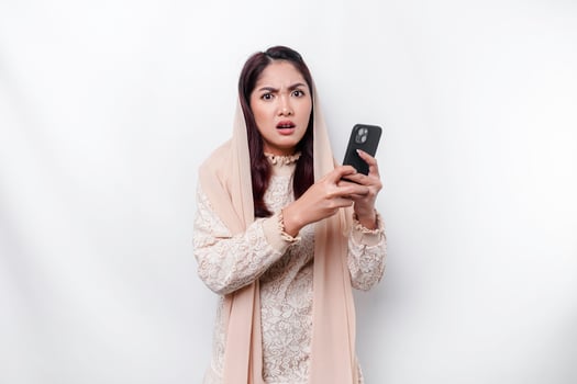 A depresses Asian Muslim woman wearing a headscarf looks stressed while talking on the phone isolated by white background photo