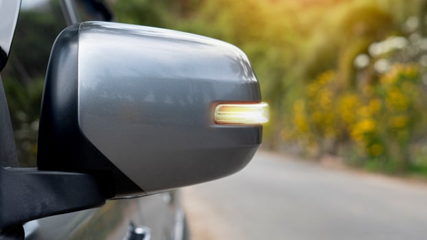 Mirror wing of gray with turn light signal. Blurred of asphalt road and trees with yellow flower for background. photo