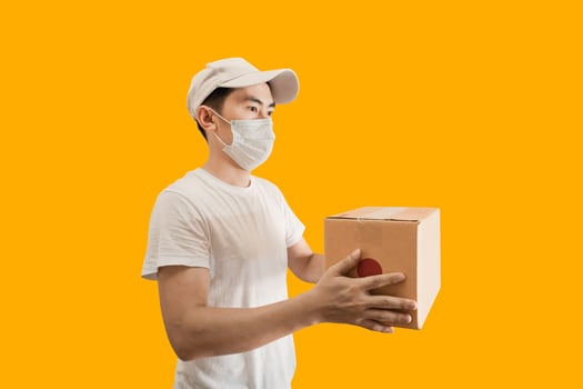 Young Asian delivery man wearing cap and white blank t-shirt holding parcel post box isolated on yellow background. express delivery service concept. photo