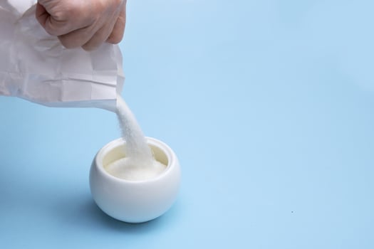 hand pours sugar into a sugar bowl on a blue background with copy space photo