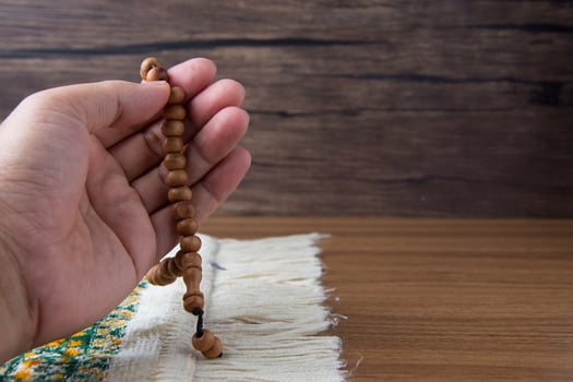 praying, palms up when praying in Islamic culture, carrying prayer beads on a prayer rug on a wooden background and there is sunshine, empty space, copy space, photo