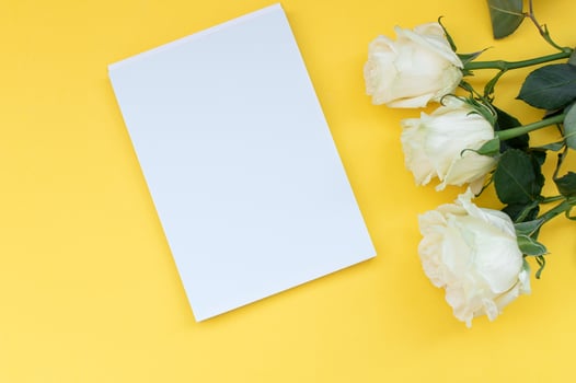 Top view of a yellow table with a mockup of empty notebooks with a bouquet of roses. Place for text photo