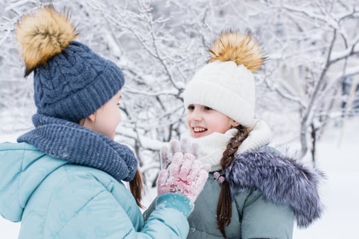 Two smiling girls in warm clothes met in a snowy park. Winter walks, lifestyle photo