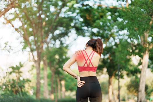 Young fitness woman holding her sports injury shoulder and neck, muscle painful during training. Asian runner female having body problem after exercise outside in summer photo