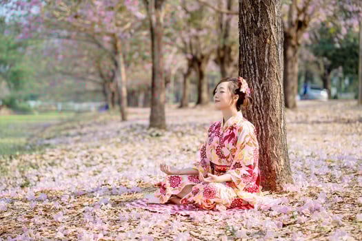 Young lady in traditional kimono dress practices meditation at cherry blossom tree. Emotion smile photo