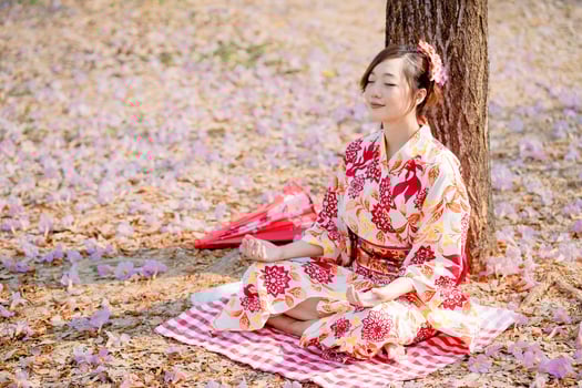 Asian woman in traditional kimono dress practices meditation at cherry blossom tree. photo