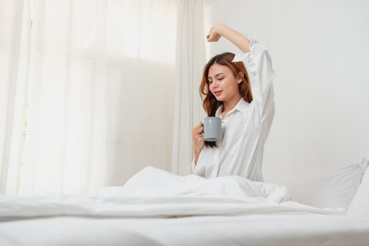 Woman in white nightgown waking up on weekend morning resting and relaxing playing with laptop mobile phone Eating bread and drinking tea in glass inside white bedroom.  Morning vacation concept. photo