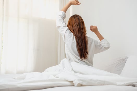 Woman in white nightgown waking up on weekend morning resting and relaxing playing with laptop mobile phone Eating bread and drinking tea in glass inside white bedroom.  Morning vacation concept. photo