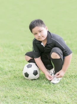 obese boy tying his football shoes, healthy concept photo