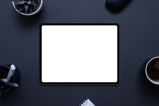 Tablet mockup on black desk with plant, pens, coffee mug, glasses box, and pad,. Top view, flat lay composition photo