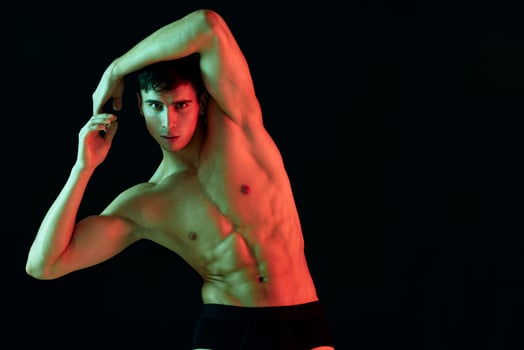 a man with a muscular physique on a black background holds his arms above his head and bent over to the side photo