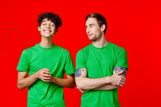 Two cheerful friends in green t-shirts communicating emotions red background photo