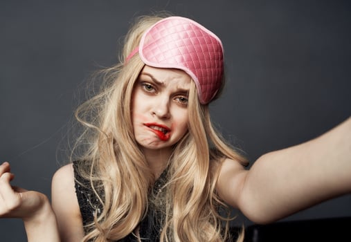 A drunken blonde with a pink sleep mask on her head smears lipstick on her face photo
