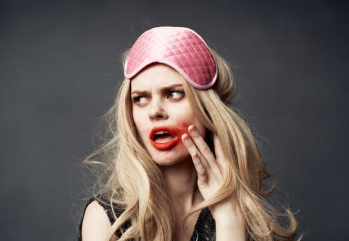 A blonde with bright makeup on her face and a pink sleep mask on her head photo