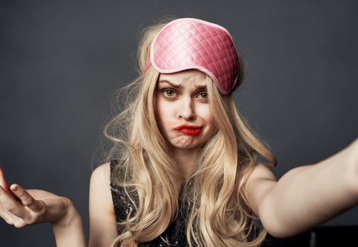A drunken blonde with a pink sleep mask on her head smears lipstick on her face photo