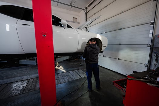 Mechanic in service repair station working with muscle car, dismantles a wheel on lift. photo