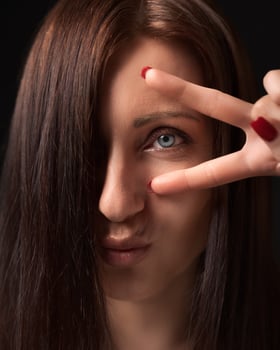 Closeup portrait woman showing victory or peace gesture with fingers near eye and looking at camera photo