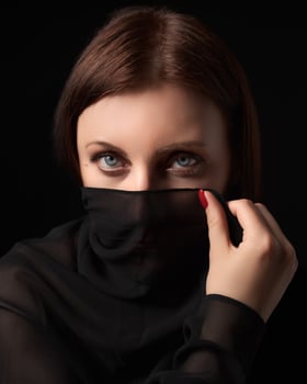 Shy brunette woman with gray eyes covered nose and mouth or face with headscarf, looking at camera photo