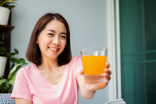 Mid-age Asian woman reading a book and hold orange juice glass in the home. Concept of  Health care And eating for healthy photo
