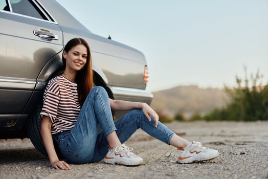 A young woman sits on the ground near her car on the side of the road and looks at the sunset. Camping after a hard road trip photo