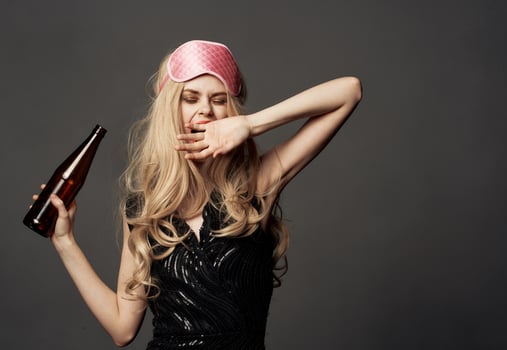 Women with a pink sleep mask holds a bottle of beer in her hand photo