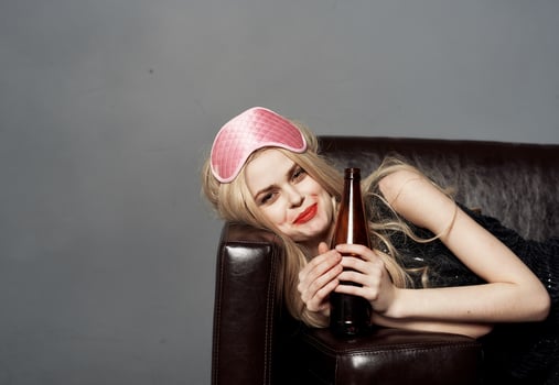 A woman with a pink mask on her head and a bottle of beer sleeps on the couch photo