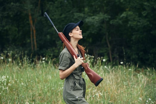 Woman on outdoor Side view of holding a weapon in the hands of a green jumpsuit black cap photo